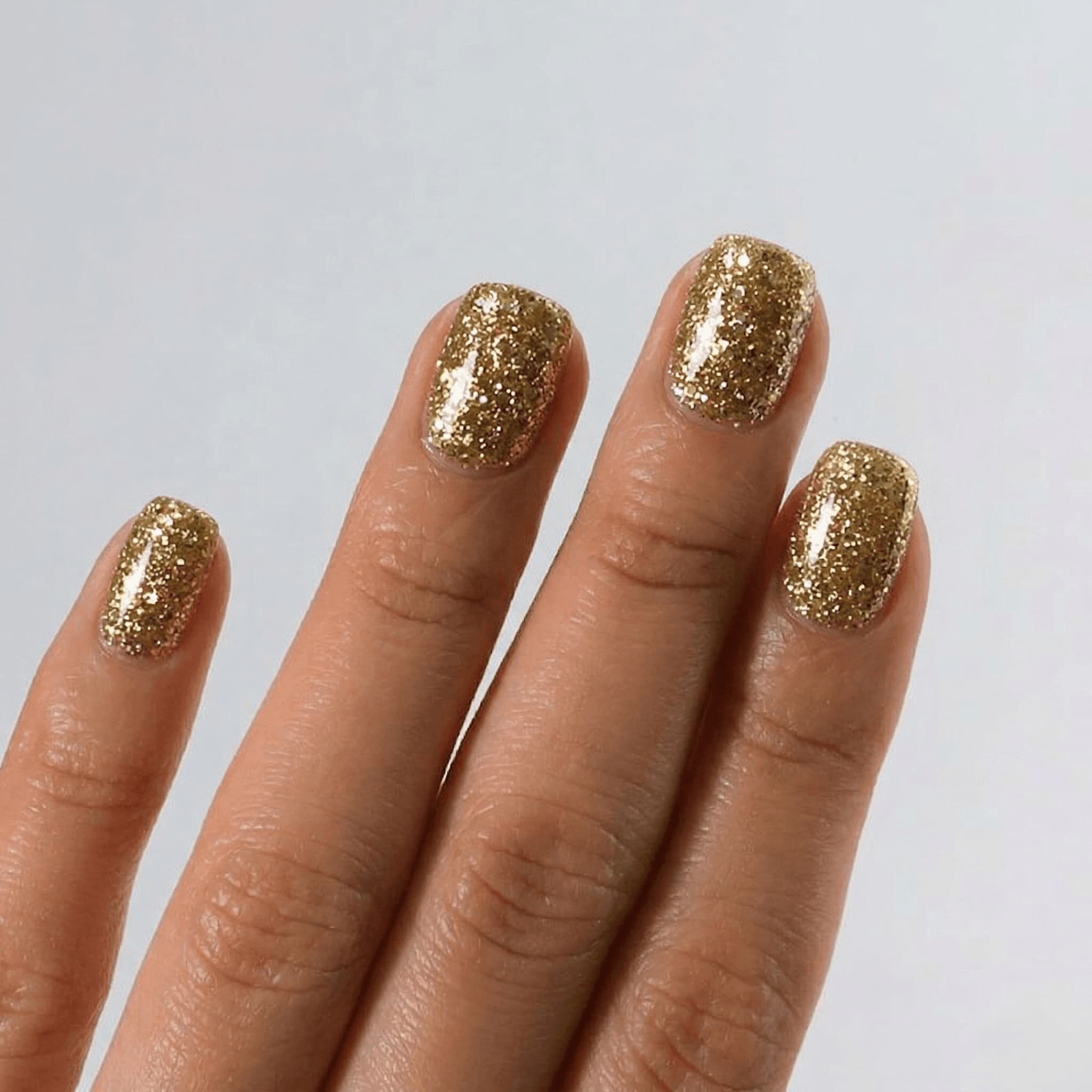 Hand with S&L gold glittery nail polish on a plain background