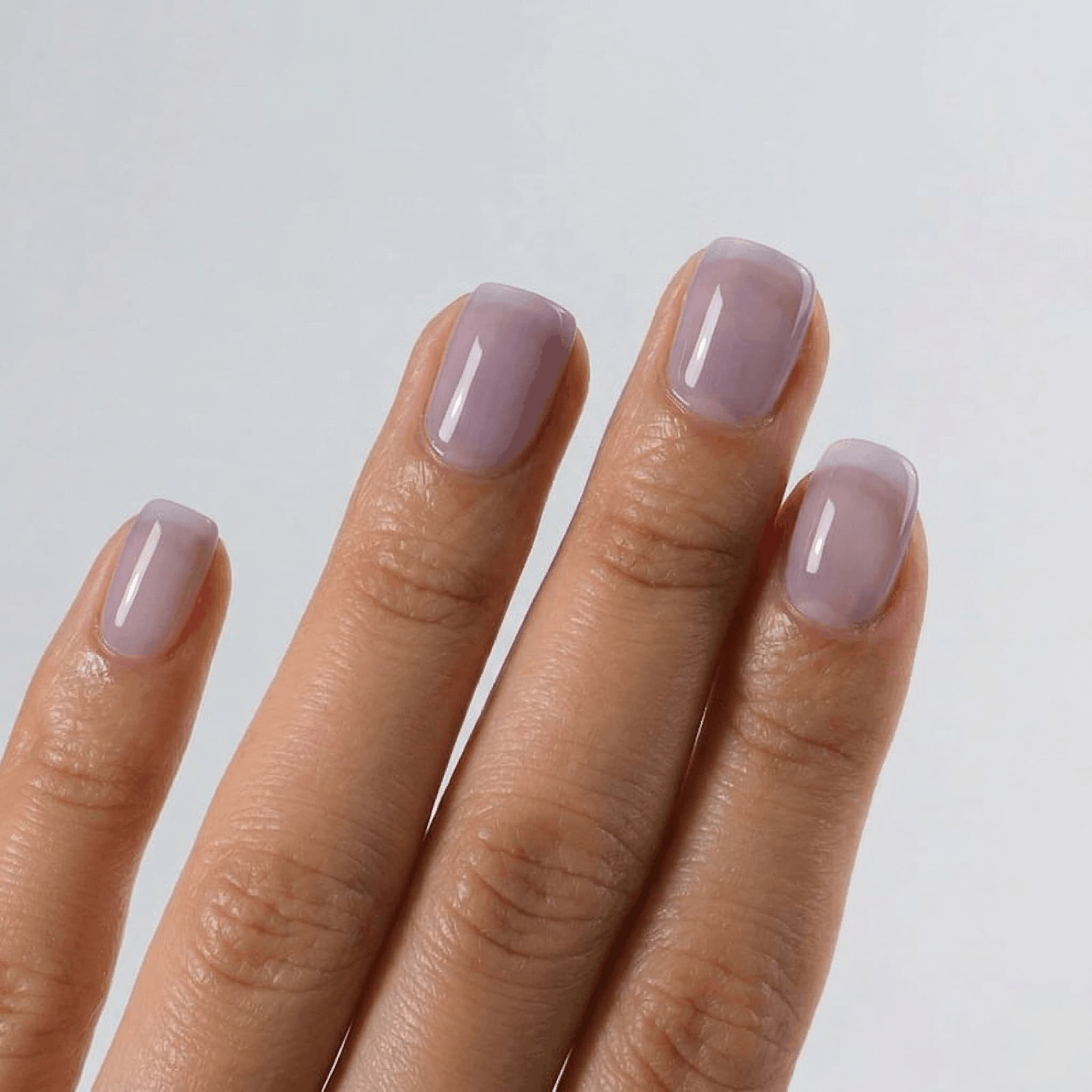 Hand with light purple nail polish on a plain background - jelly finish