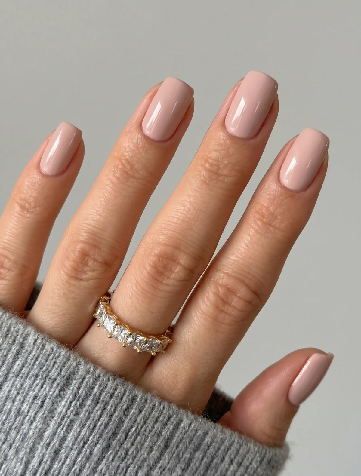 S&L Beauty Co. Gel Nail Polish No. 017 Beauty Bush applied on short, square-rounded natural nails, featuring an opaque, glossy soft blush pink finish paired with a grey knit sweater cuff.