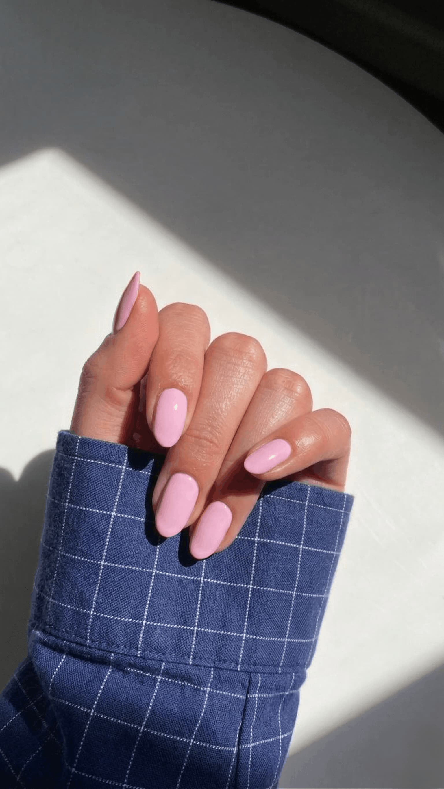 Hand with pink nail polish wearing a blue checkered sleeve against a light background