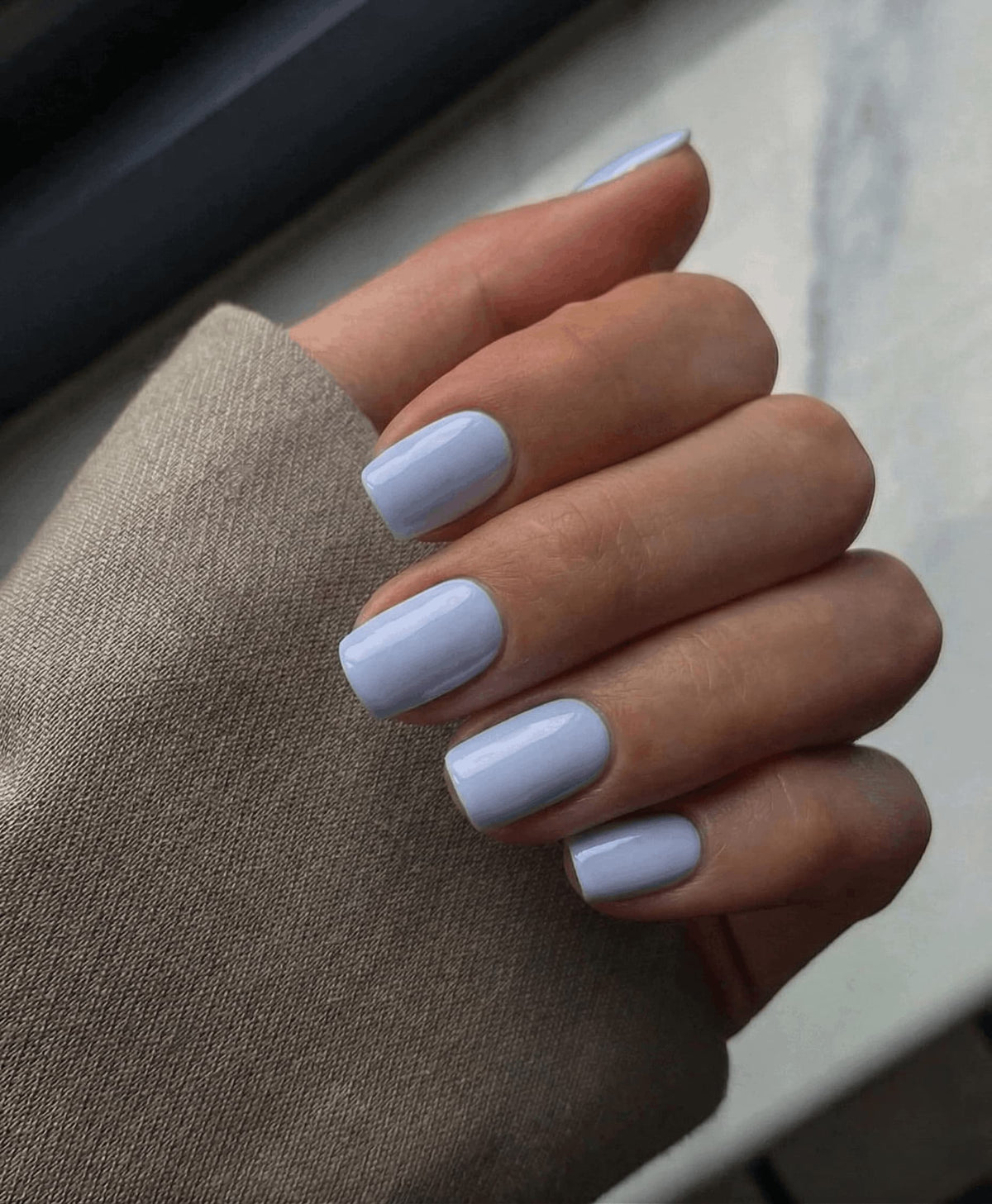Hand with light blue nail polish on a neutral background