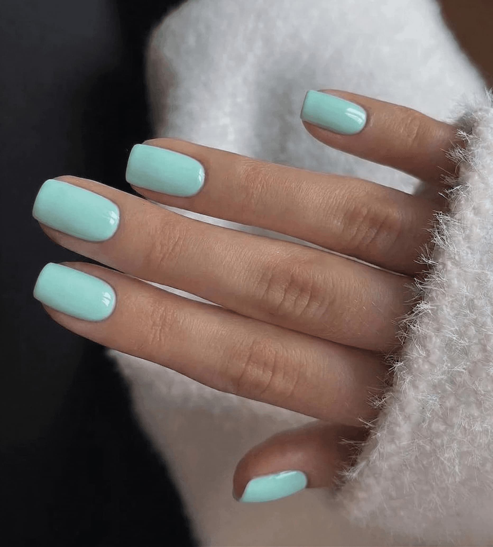 Close-up of a hand with light blue nail polish on a blurred background