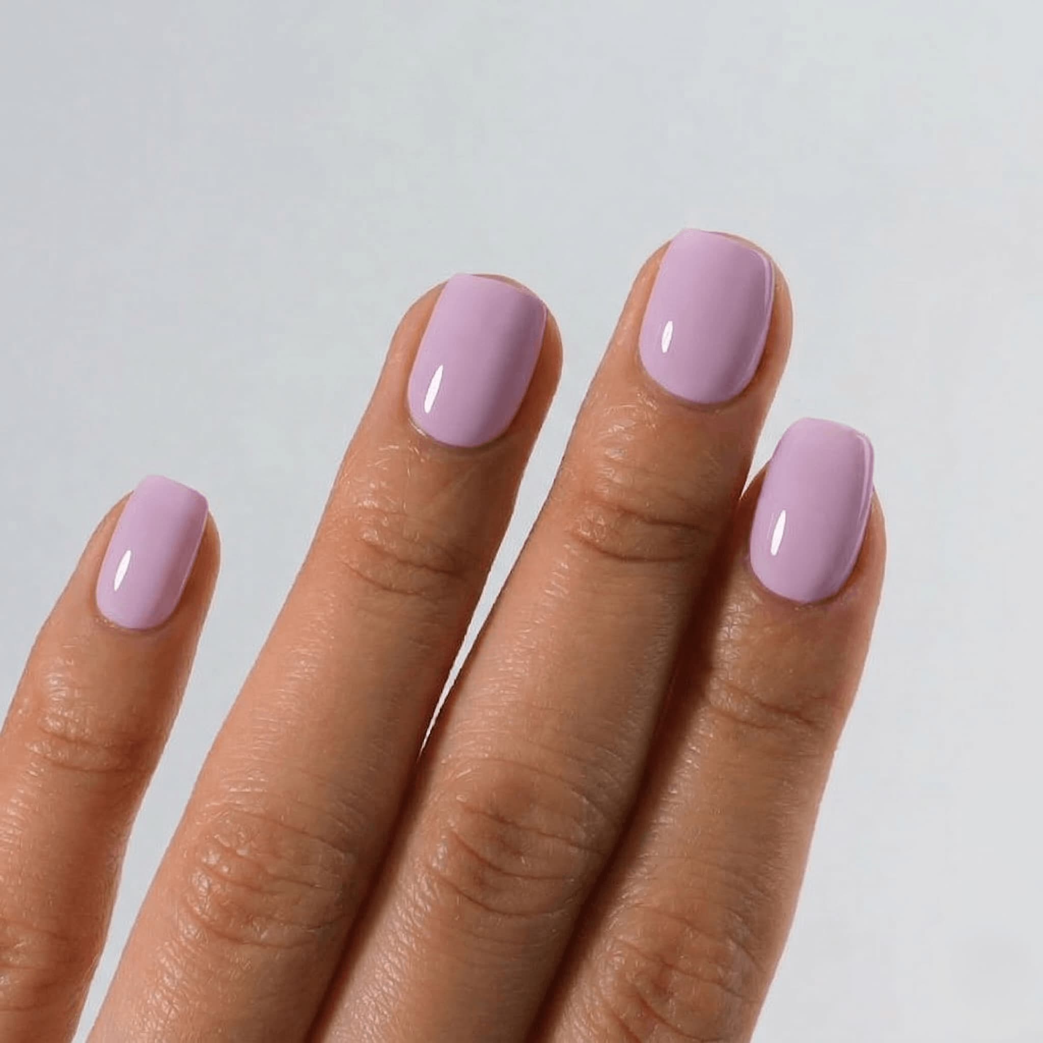 Hand with light purple nail polish on a plain background