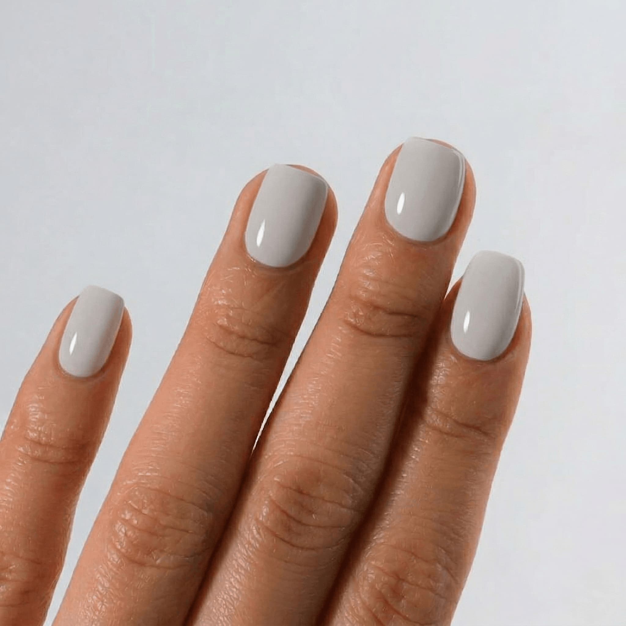 Hand with light gray nail polish on a plain background