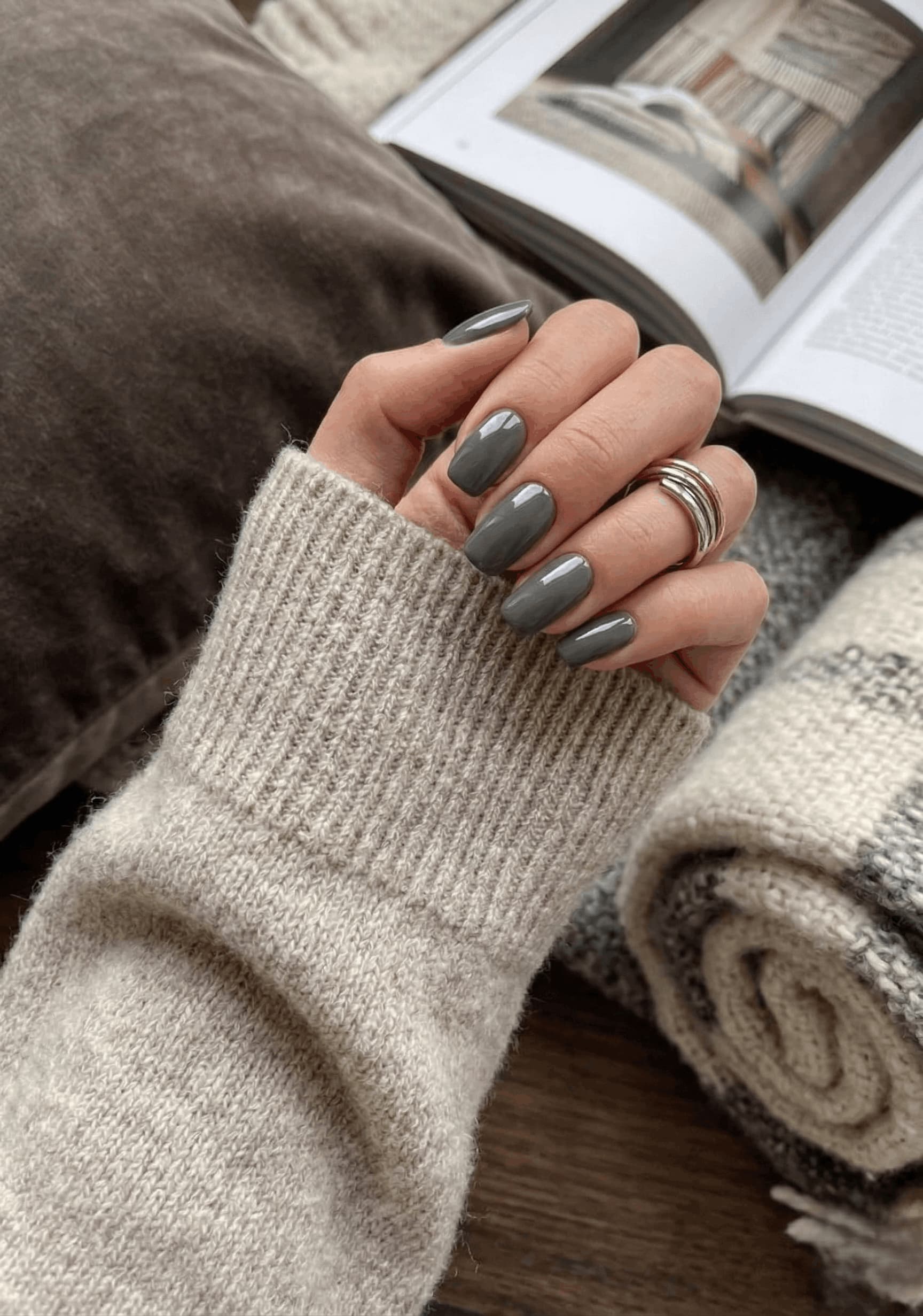 Person wearing a beige sweater with gray nail polish and rings, holding a book.