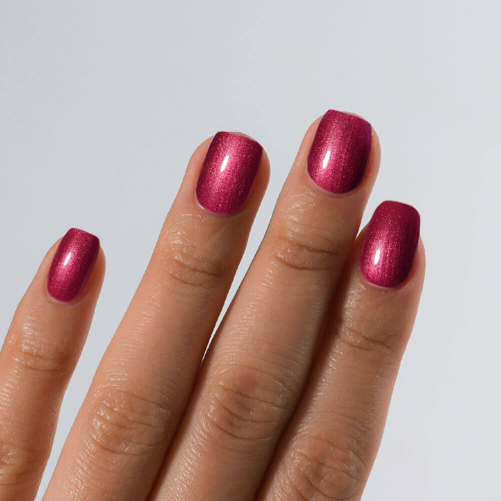 Hand with S&L red metallic nail polish on a light gray background