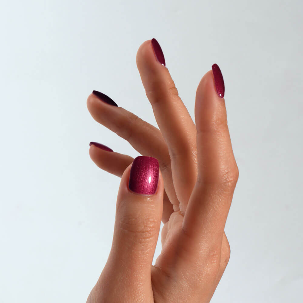 Hand with S&L red metallic nail polish on a light gray background