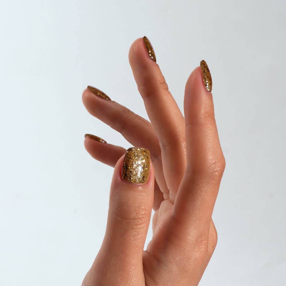 Hand with S&L gold glittery nail polish on a plain background