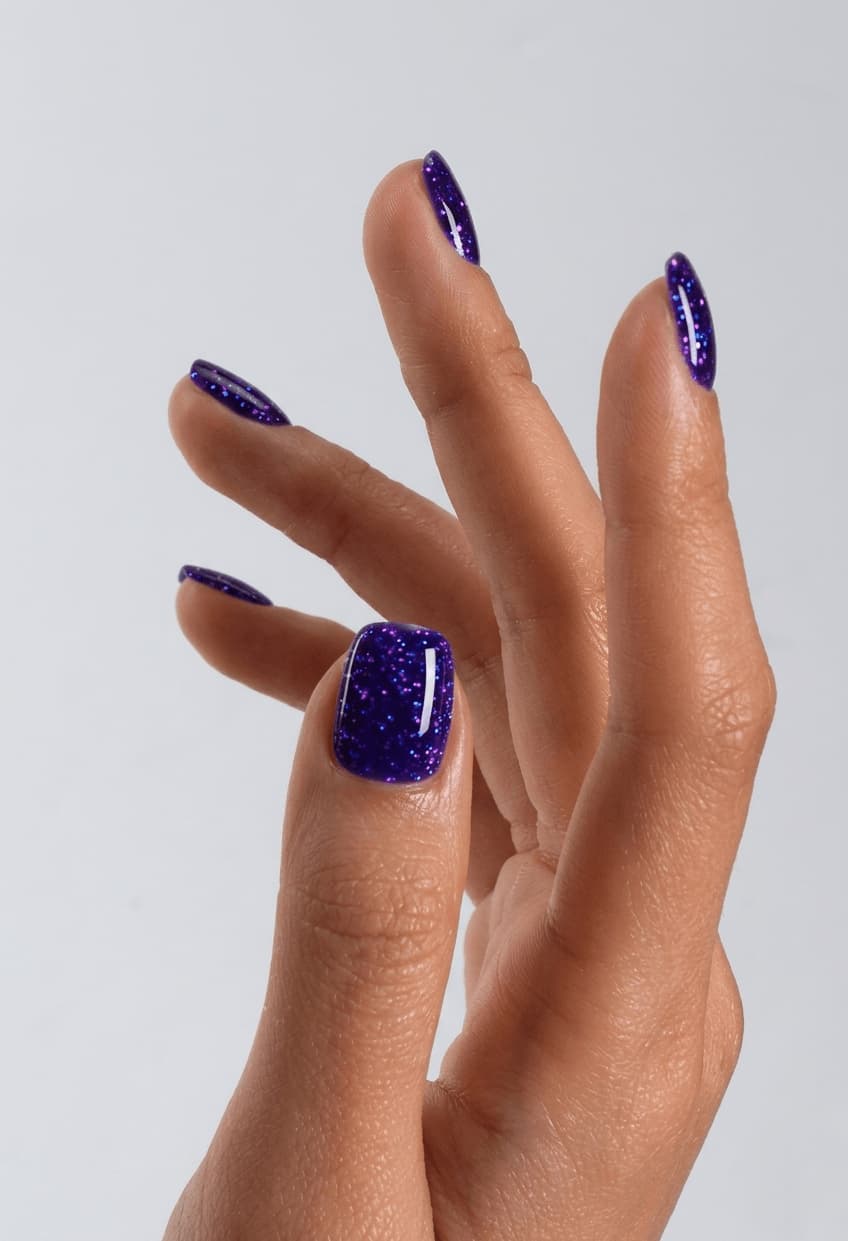Hand with S&L purple glittery nail polish on a plain background