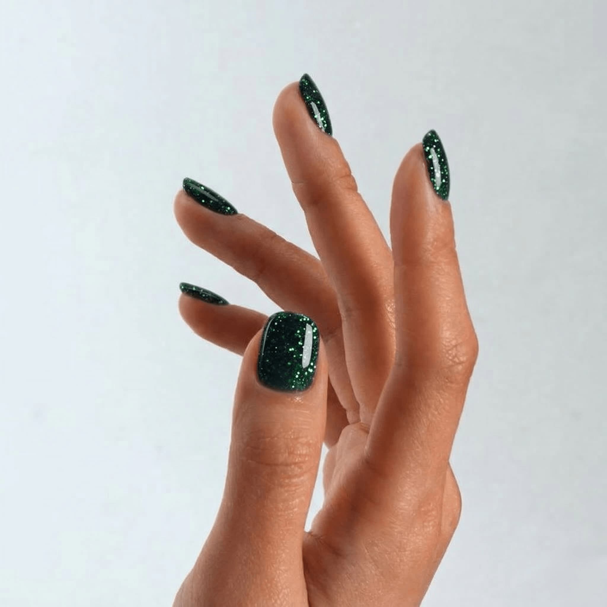Hand with S&L green glittery nail polish on a plain background
