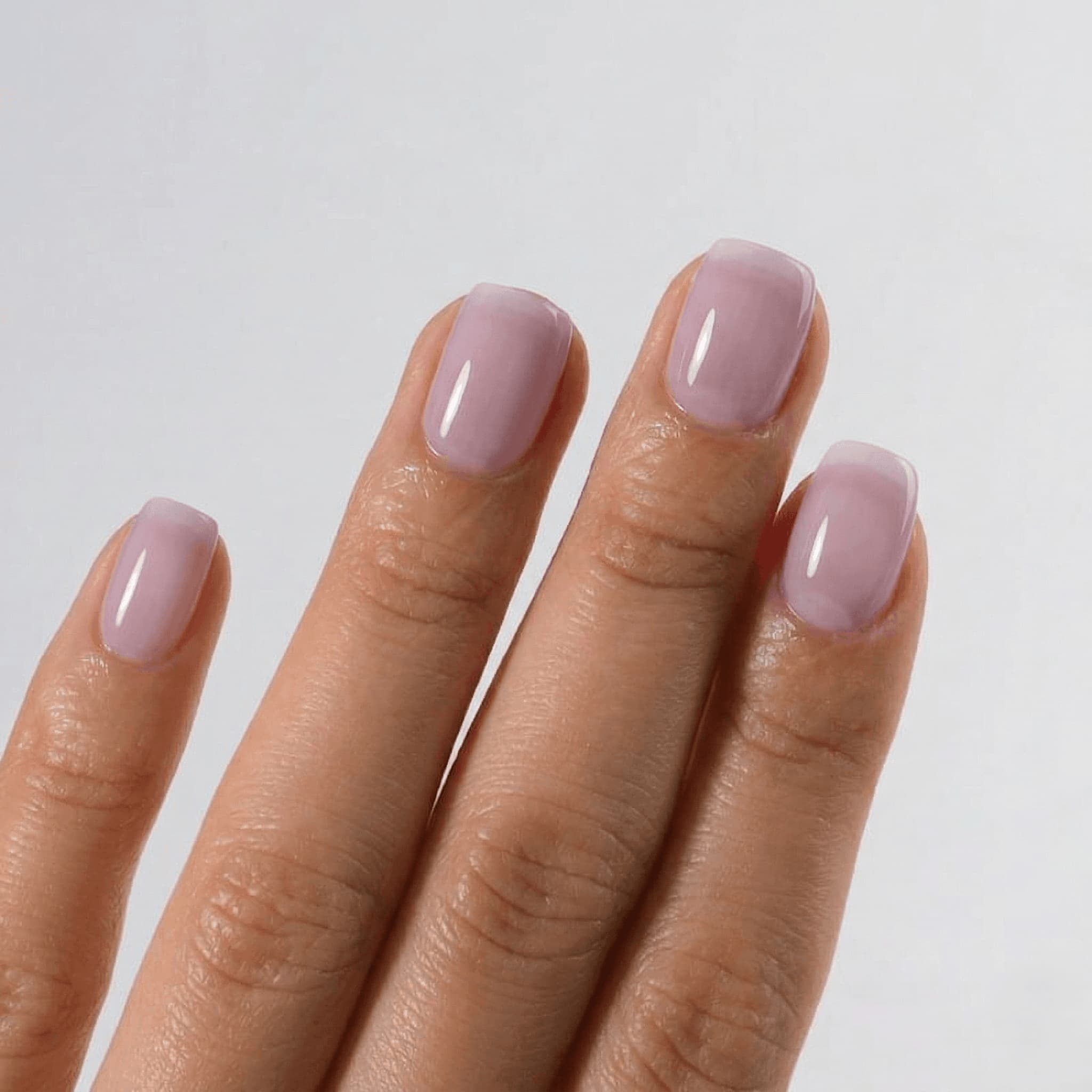 Hand with light pink nail polish on a plain background