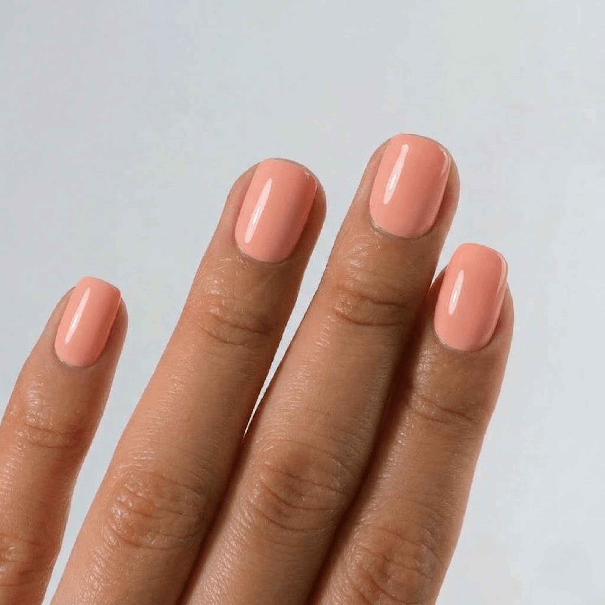 Hand with coral nail polish on a plain background