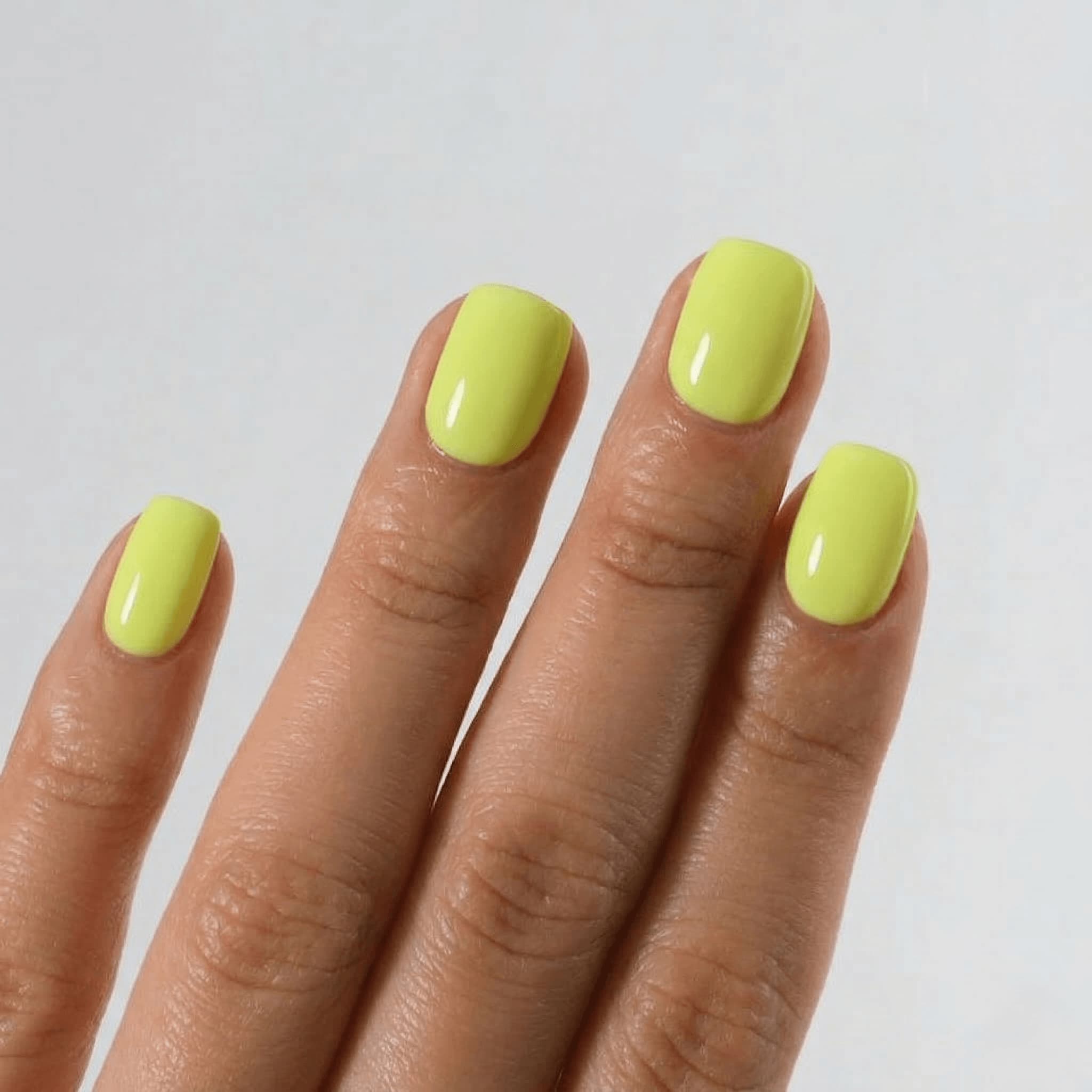 Hand with bright yellow nail polish on a plain background