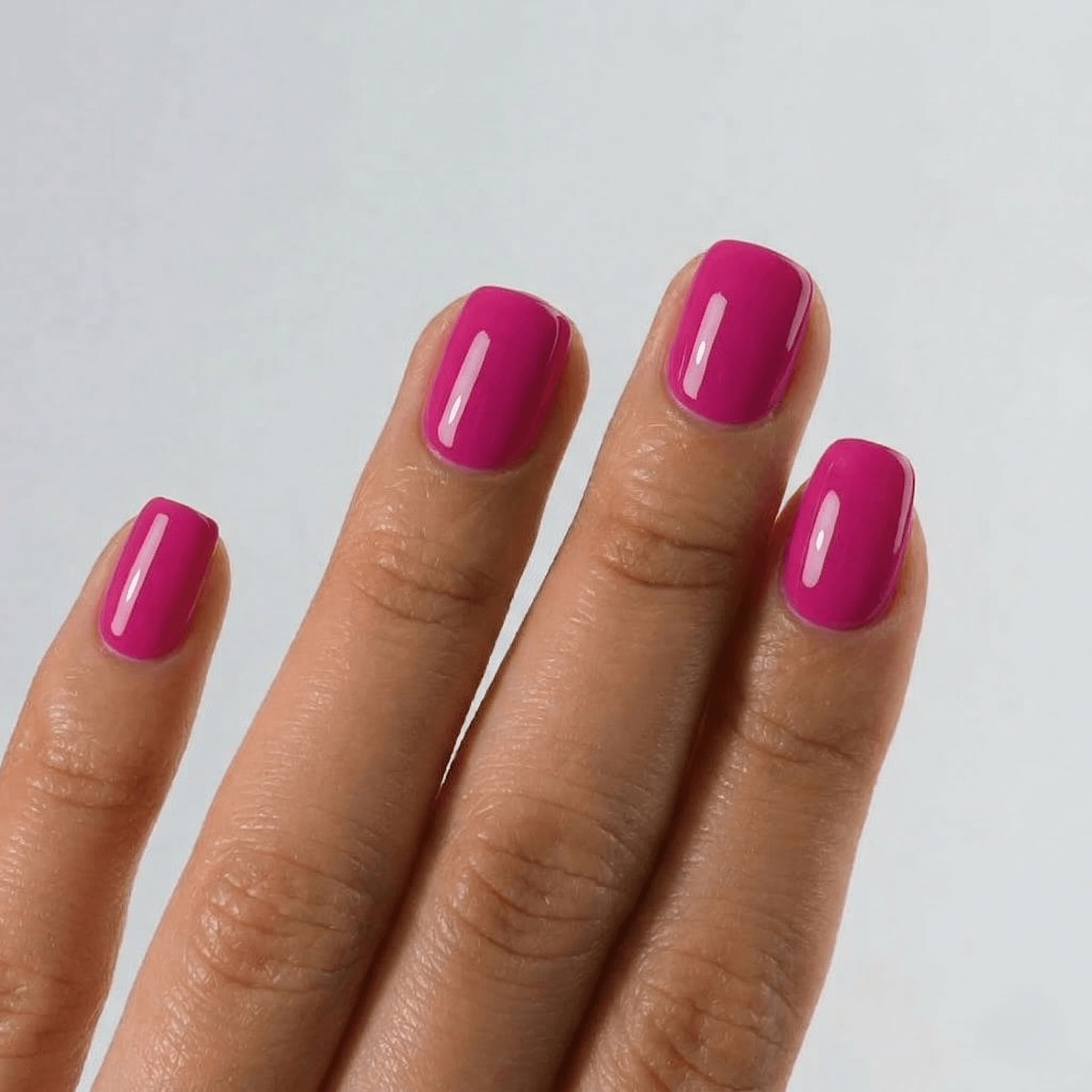 Hand with bright pink nail polish on a plain background