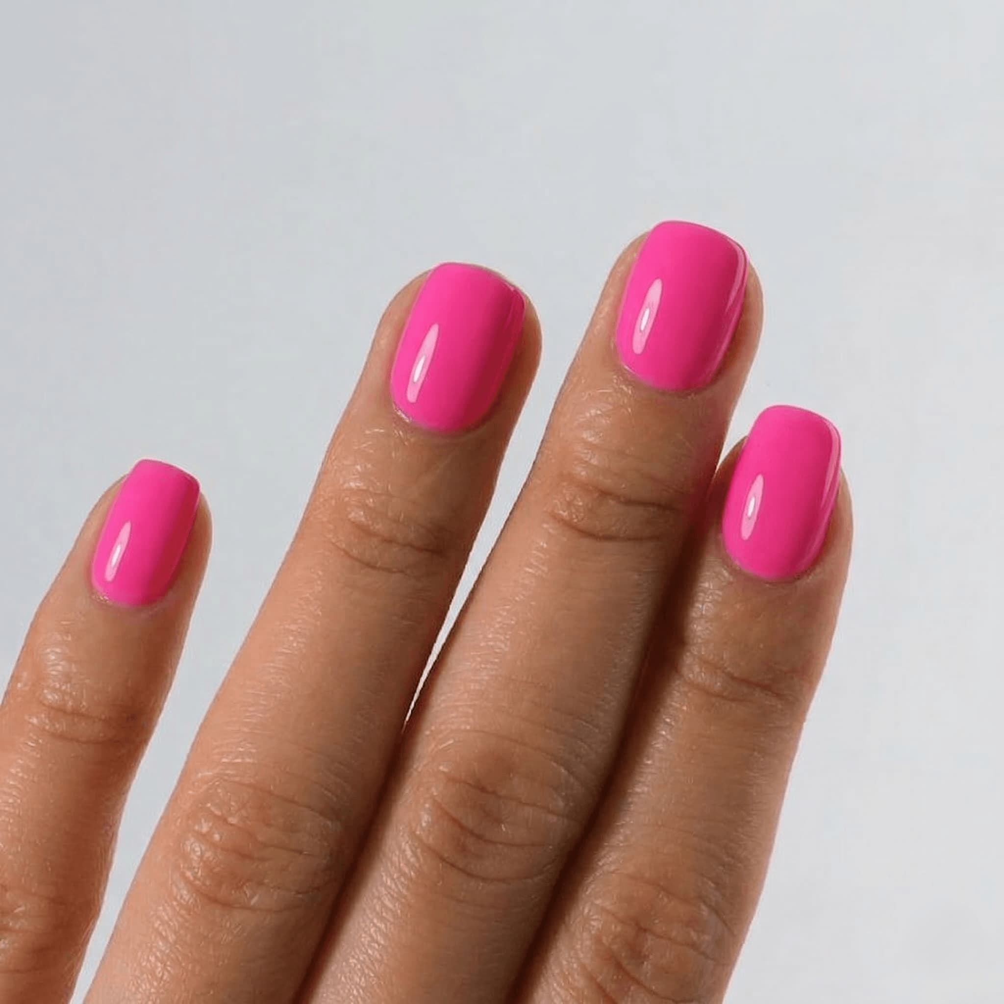 Hand with neon bright pink nail polish on a light gray background