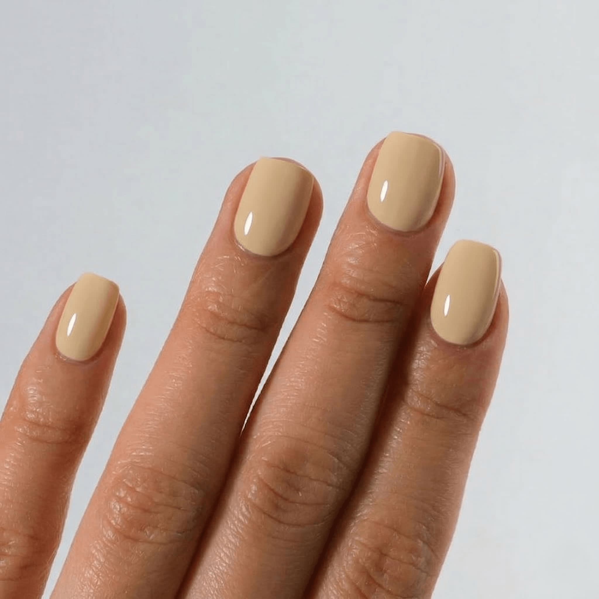 Hand with beige nail polish on a plain background