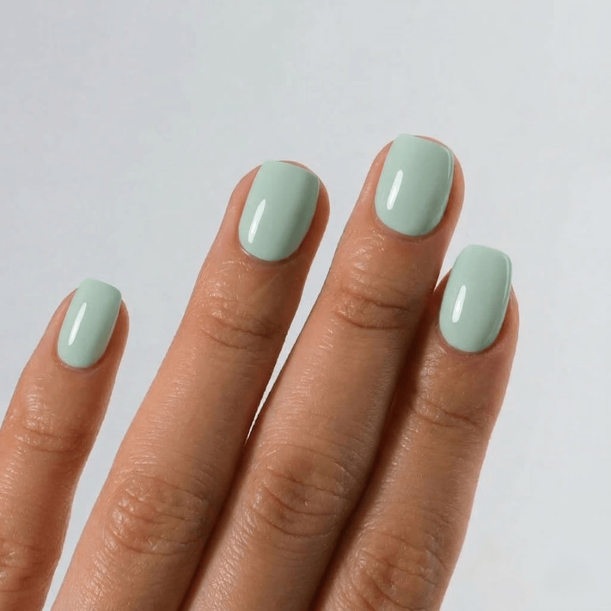 Hand with light green nail polish on a plain background