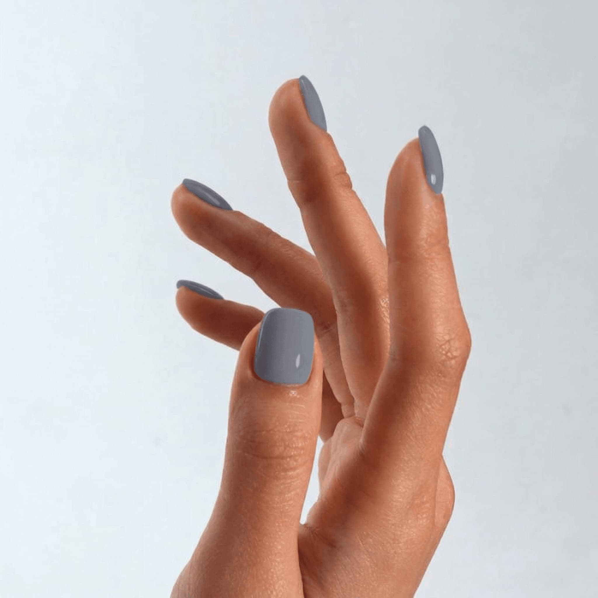 Hand with gray nail polish on a light gray background