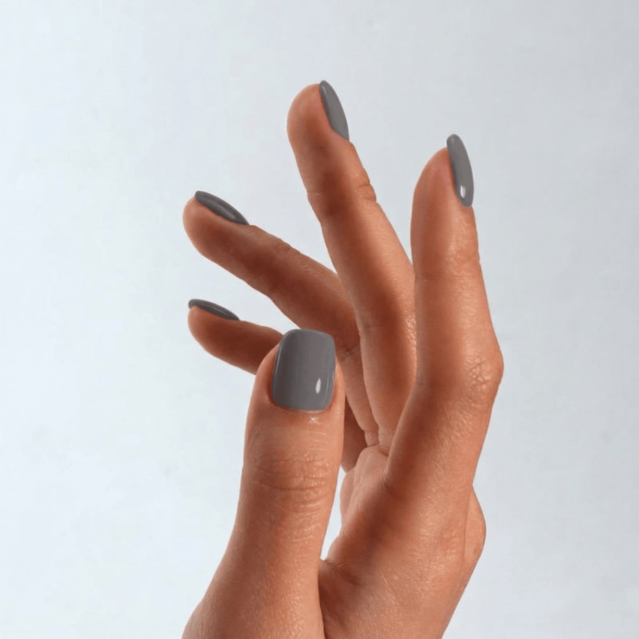 Hand with gray nail polish on a light gray background
