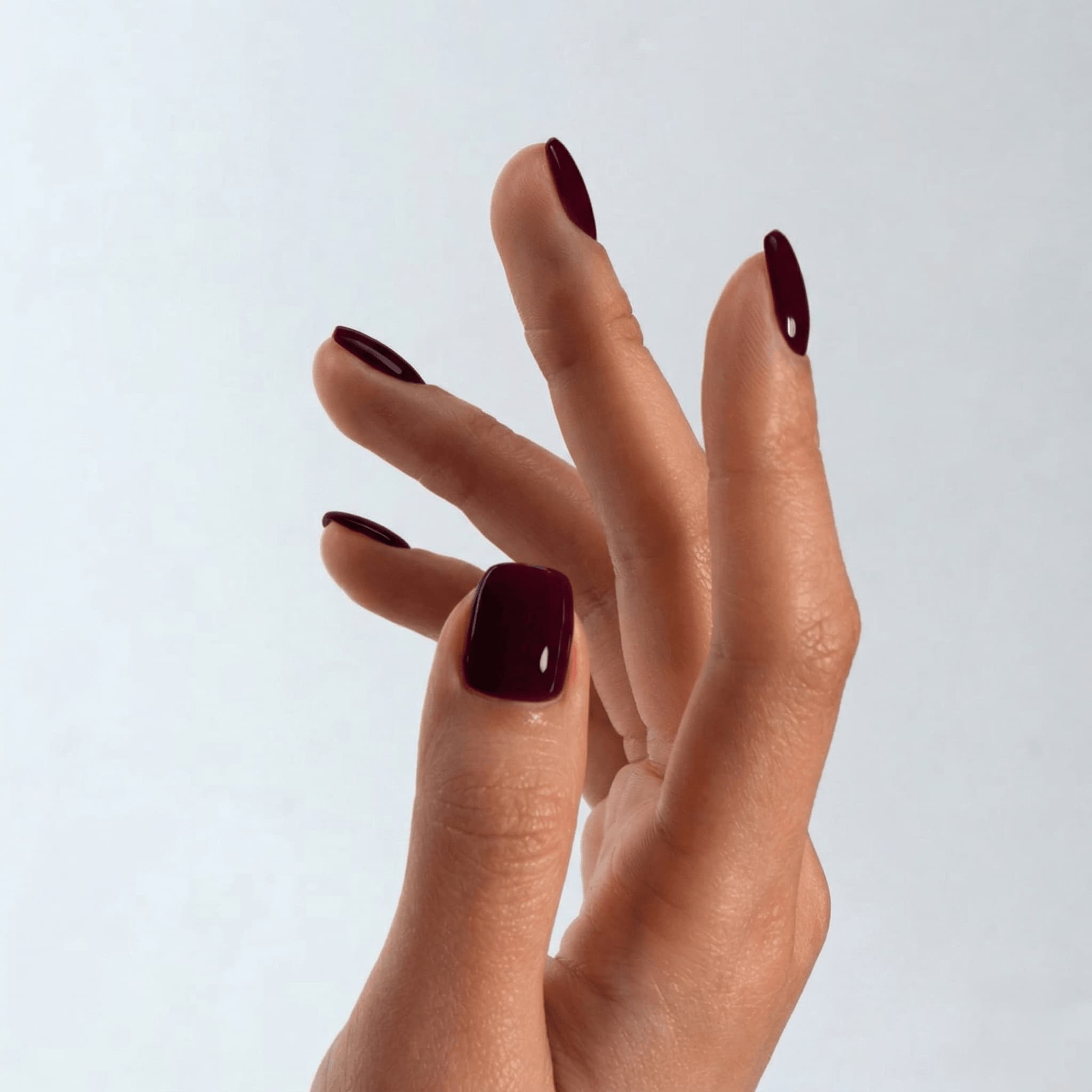 Close-up of a hand with dark red nail polish on a light gray background