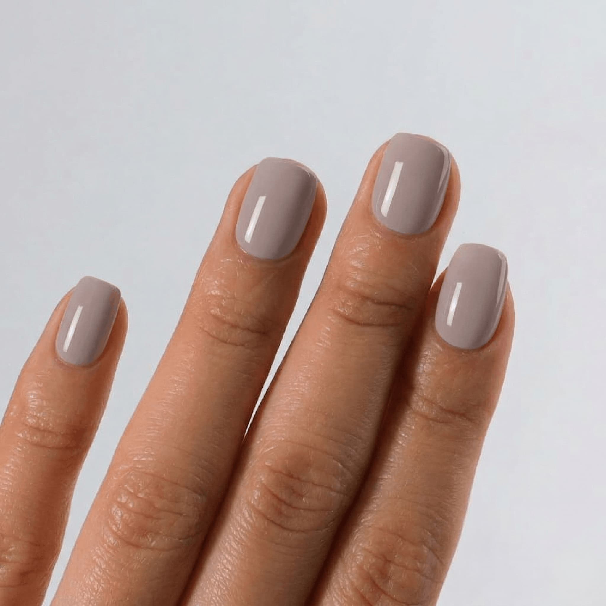Hand with S&L beige nail polish on a light gray background