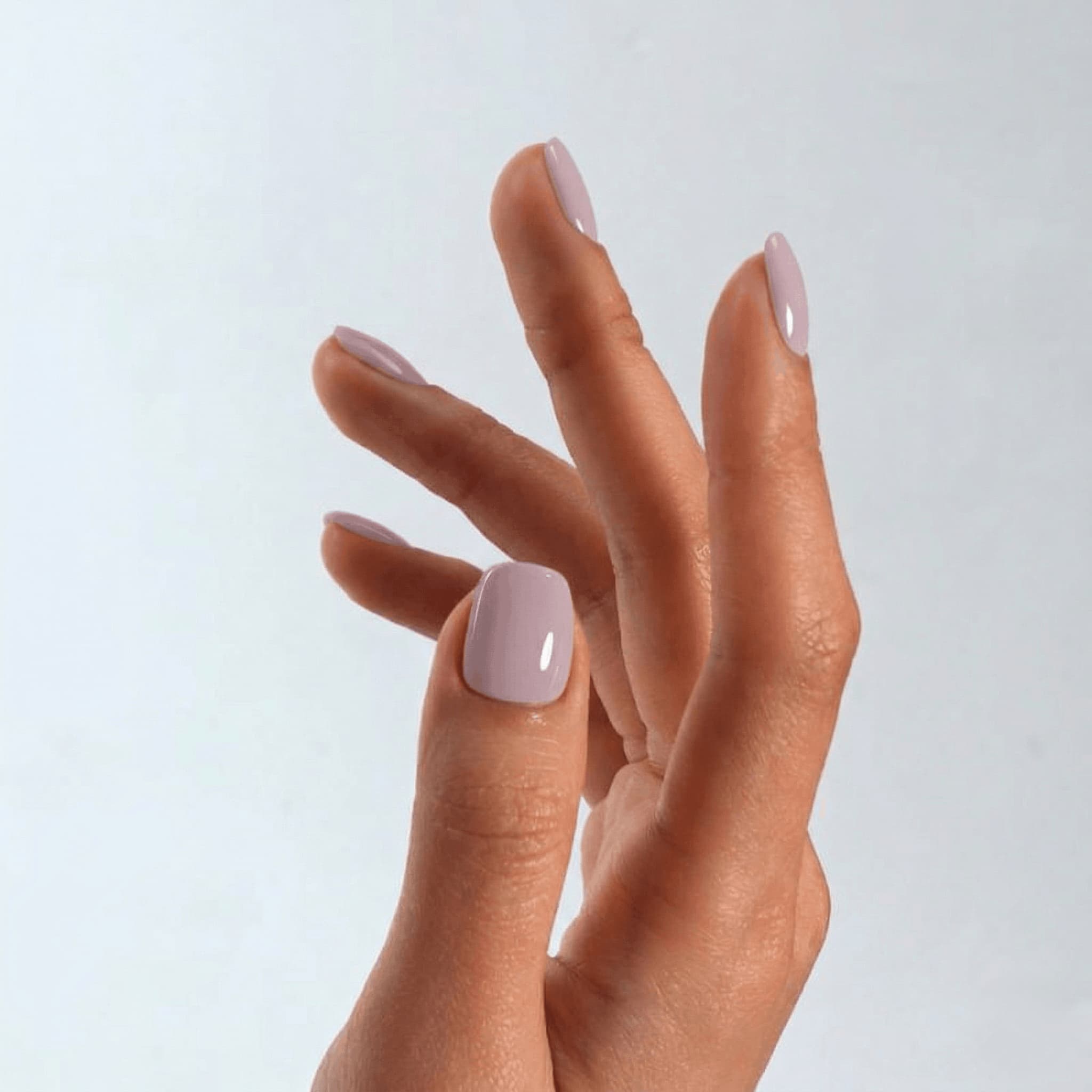 Close-up of a hand with S&L light pink nail polish on a light gray background