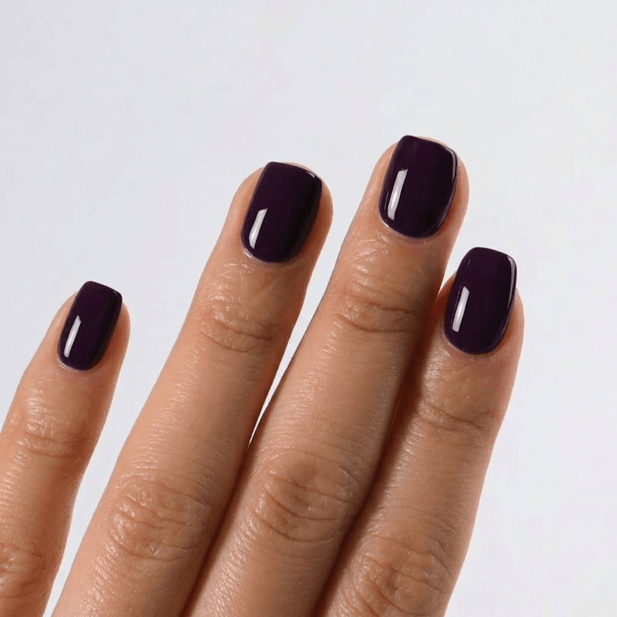 Hand with dark purple nail polish on a light gray background