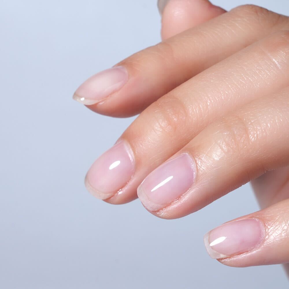 Close-up of a hand with soft builder gel and pink nail polish on a light blue background