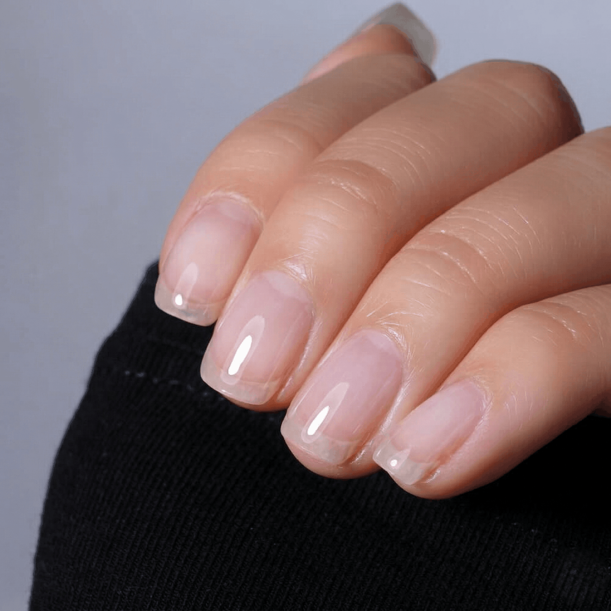 Close-up of a hand with builder gel and faint pink nail polish on a neutral background