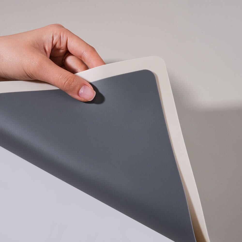 Close-up of a hand lifting a flexible silicone nail mat in grey and beige, showing easy handling for nail art cleanup