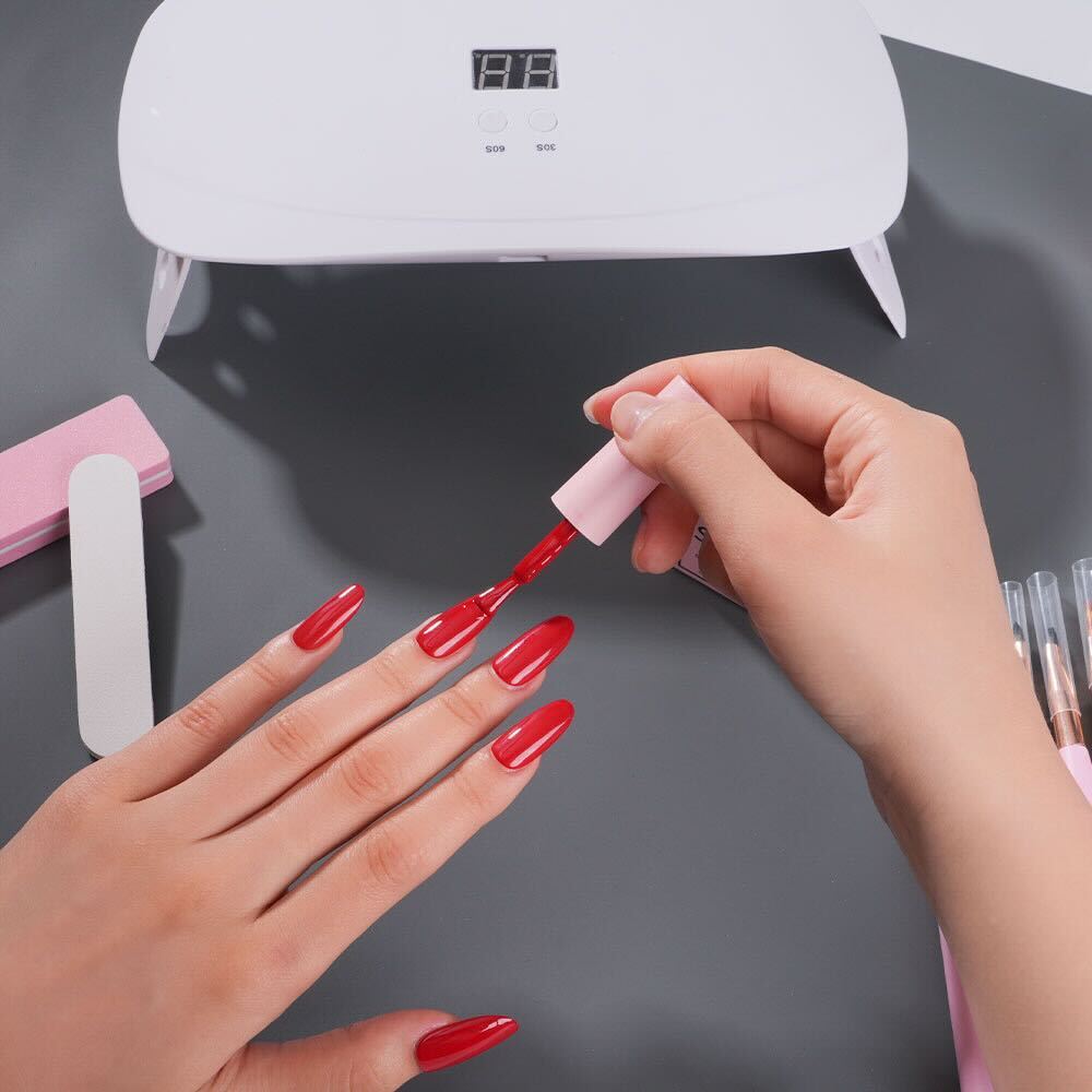 Applying red gel polish on nails over a grey silicone nail mat with manicure tools and UV lamp