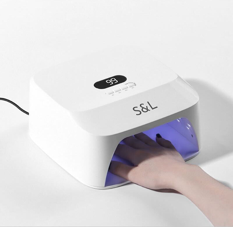 A hand inside the S&L 48W UV LED nail lamp during curing, with digital timer and soft purple light on white background