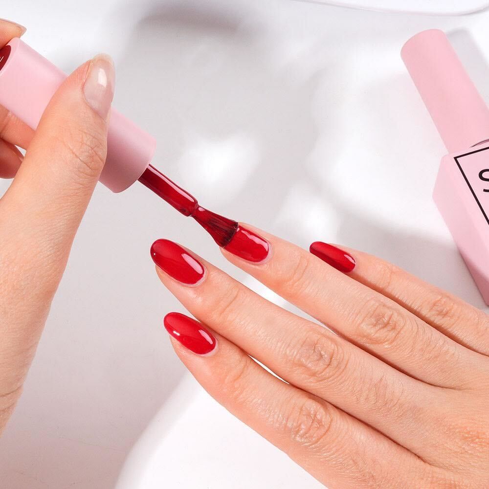 Close-up of a hand applying S&L red gel nail polish from the starter kit onto fingernails at home